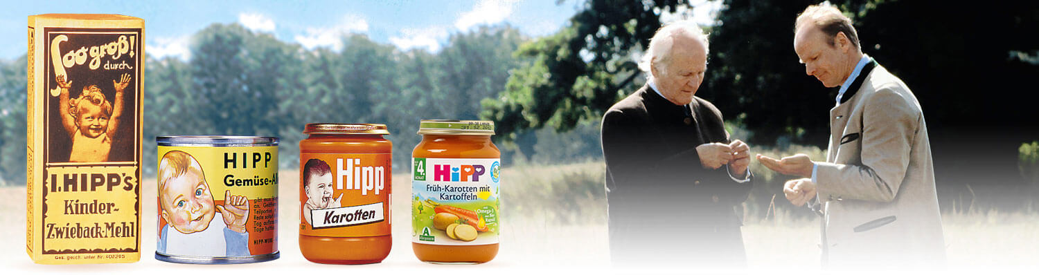 Two men are engaged in a conversation outdoors, with three containers of baby food products displayed in the foreground.
