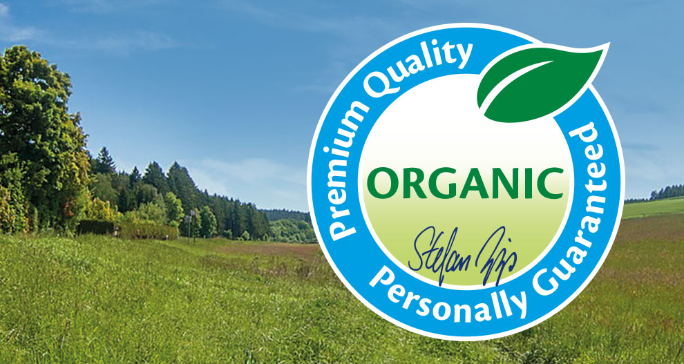 A landscape with green grass and trees is overlaid with a blue circular graphic containing the word “ORGANIC” and a signature.