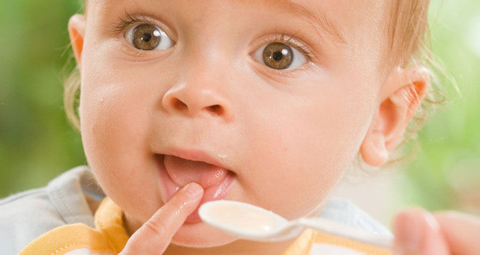 A close-up of a baby's face, with a spoonful of food near the mouth, captured in a candid moment.