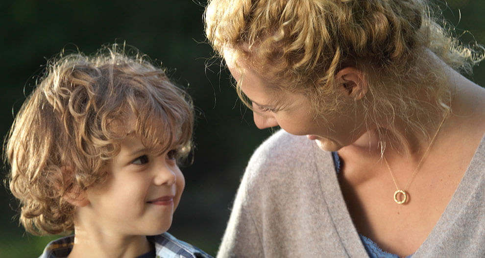A woman and a young boy are engaged in a close, intimate moment outdoors.