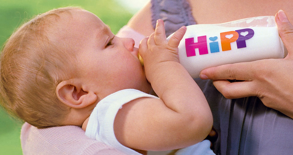 A baby drinks from a bottle with the word "HiPP" on it.