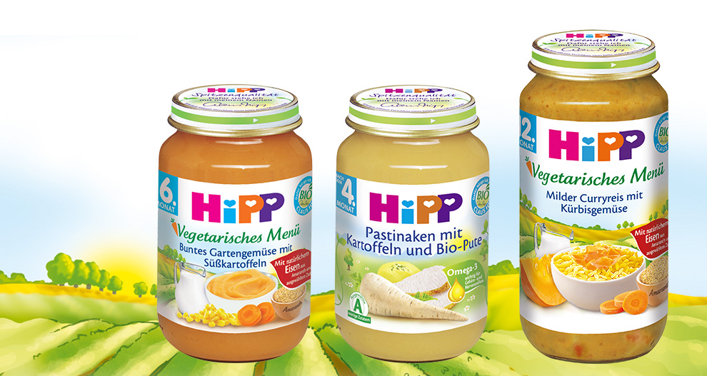 Three Hipp baby food jars with different labels are displayed against a green landscape background.