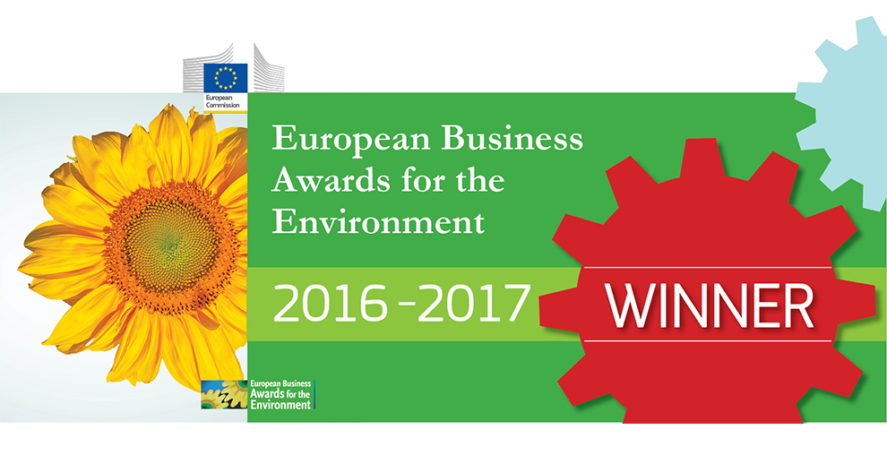 A sunflower on the left, a green banner with the text "European Business Awards for the Environment 2016-2017" in the center, and a red gear shape on the right with the word "WINNER" inside it.